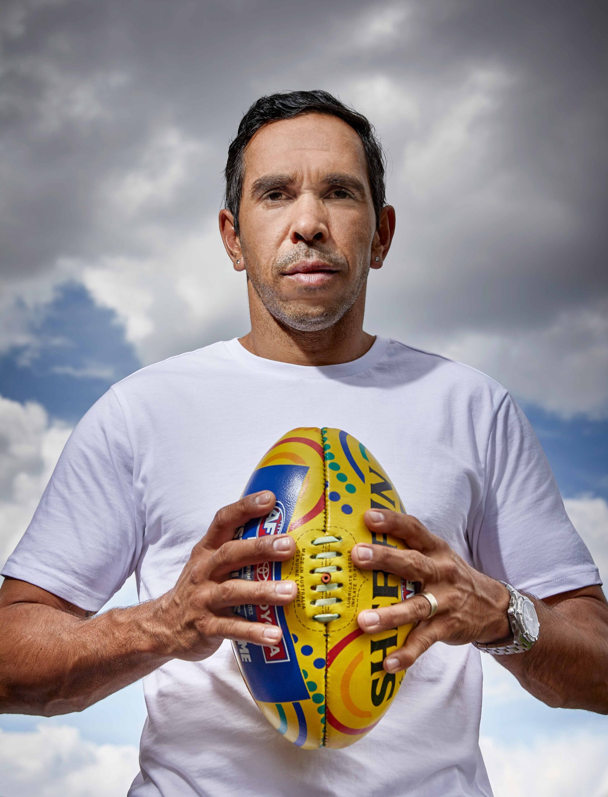 Footballer Eddie Betts holds a football and looks down at the camera 